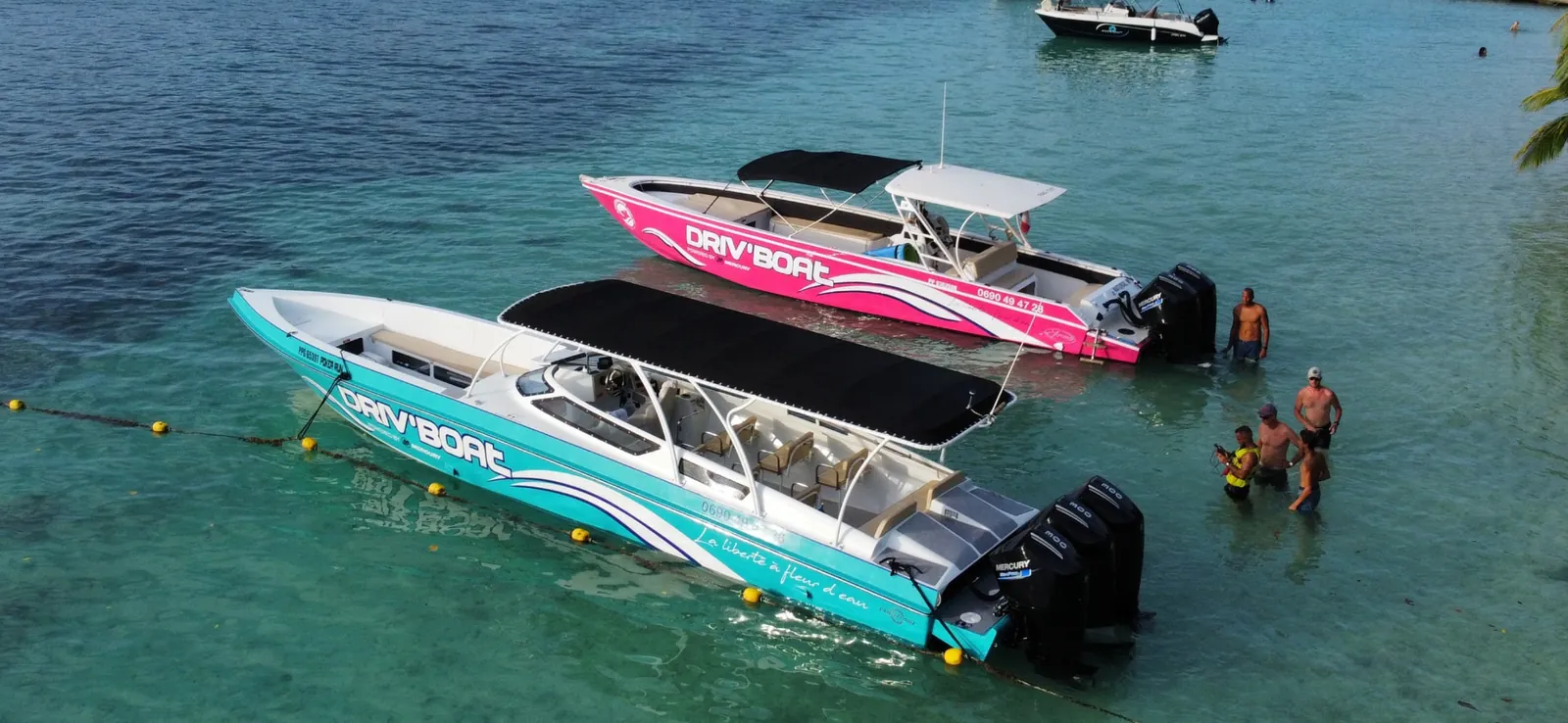 Deux bateaux Driv'Boat amarrés dans une eau turquoise peu profonde, vus du ciel, équipe debout dans l'eau à l'arrière
