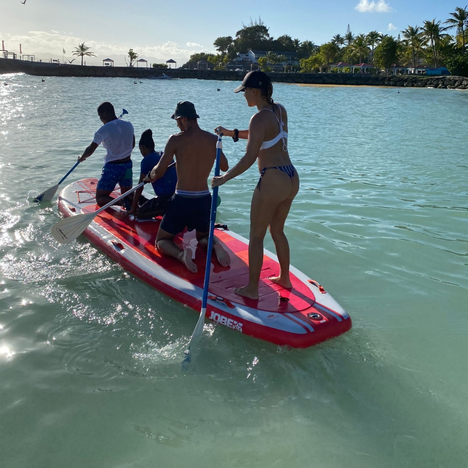 Quatre amis sur un stand up paddle géant Jobe, sur une eau turquoise devant une plage de cocotiers