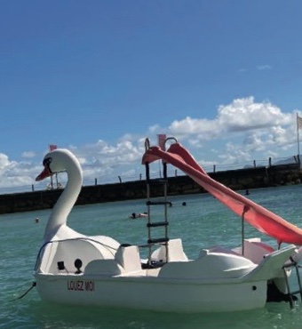 Pédalo blanc en forme de cygne avec un toboggan rose près de la plage, activité nautique au Gosier
